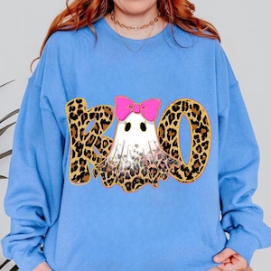 Könnte beinhalten: Ein hellblaues Sweatshirt mit Rundhalsausschnitt und einem Grafikdruck des Wortes BOO. Die Buchstaben B und O sind mit einem braun-schwarzen Leopardenmuster gefüllt. Ein weißes Gespenst mit einer leuchtend rosa Schleife sitzt zwischen den Buchstaben.
