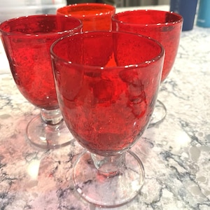 Puede incluir: Juego de cuatro copas de vino rojas con una textura similar a burbujas. Las copas tienen un diseño clásico con pie, base transparente y un tono rojo vibrante, perfectas para servir vino u otras bebidas.