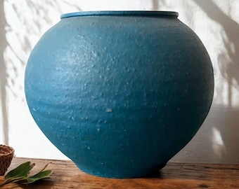 May include: A large, round, teal blue ceramic vase with a smooth, textured surface.