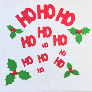Pode incluir: Letras de feltro vermelho que soletram "HO HO HO" com letras menores que soletram "HO" espalhadas ao redor. Folhas de azevinho de feltro verde com bagas vermelhas espalhadas ao redor das letras.