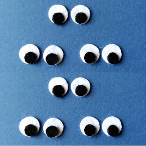 May include: Eight white googly eyes with black pupils arranged in three rows on a blue background.
