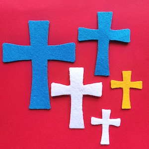 May include: A collection of felt crosses in various sizes and colors, including blue, white, and yellow, arranged on a red background. The crosses are cut from felt and have a simple, symmetrical design.