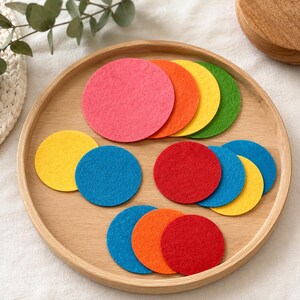 Könnte beinhalten: Eine Sammlung runder Filzuntersetzer in verschiedenen leuchtenden Farben wie Rot, Orange, Gelb, Grün und Blau. Diese flachen, runden Filzteile sind auf einem kreisförmigen Tablett aus hellem Holz angeordnet und zeigen eine Vielfalt an Farben.