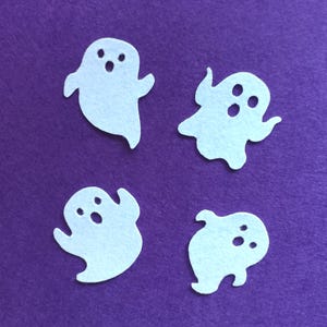 Könnte beinhalten: Vier weiße Filz-Geister-Ausschnitte auf einem violetten Hintergrund. Die Geister haben einfache Gesichtszüge, darunter Augen und einen Mund.