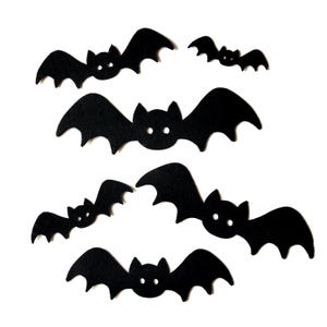 May include: A set of six black felt bats with simple, rounded wings and white eyes. The bats are arranged in a random pattern on a white background.