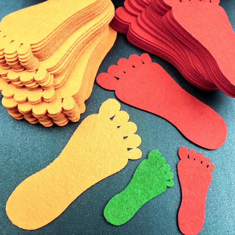 May include: A collection of die-cut felt shapes in the form of human footprints. The set includes multiple stacks and individual pieces in vibrant orange, bright red, and lime green colors, featuring distinct toe and heel outlines.