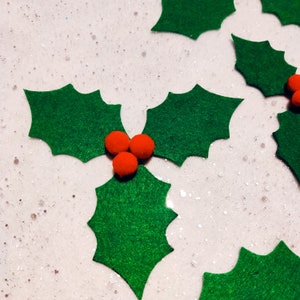 Könnte beinhalten: Drei grüne Filz-Stechpalmenblätter mit drei roten Filzbeeren in der Mitte.