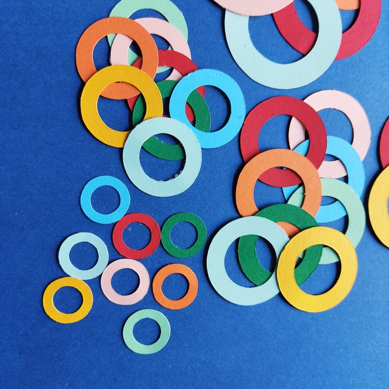 May include: A collection of colorful paper circles in various sizes and shades of red, orange, yellow, green, blue, and turquoise. The circles are arranged in a random pattern on a blue background.