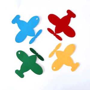 May include: Four colourful airplane cutouts in blue, red, green, and yellow. Each plane has a propeller and a small hole near the top. The planes are arranged on a white background.