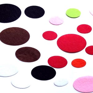 May include: A selection of colourful, oval-shaped felt pieces scattered on a white surface. The felt pieces are in various colours, including black, brown, red, pink, green, white, and orange. These craft supplies are ideal for DIY projects.