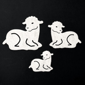 Può includere: Tre ritagli di agnelli bianchi con contorni neri su sfondo nero. Gli agnelli sono raffigurati a riposo, con dettagli come la lana riccia e i lineamenti del viso. L'immagine è una vista dall'alto.