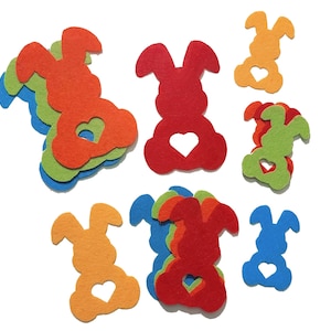 Op de afbeelding: Een set van vilt konijnenvormen in verschillende kleuren, waaronder rood, oranje, groen, blauw en geel. Elk konijn heeft een hart dat uit het midden is geknipt.