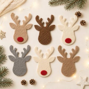 May include: Six felt reindeer head cutouts arranged in two rows. The top row features tan, dark brown, and cream reindeer, each with a red felt nose. The bottom row includes gray, off-white, and light brown reindeer, with the center one having a red nose.