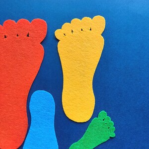 May include: Four felt cutouts in the shape of human feet arranged on a blue surface. The shapes include a large red foot, a medium yellow foot, a small blue foot, and a smaller green foot, each featuring distinct toe and heel outlines.