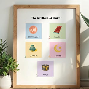 May include: A framed print titled "The 5 Pillars of Islam." The artwork features five illustrated squares with Arabic text and English translations: Shahadah, Salah, Zakah, Sawm, and Hajj. The frame is made of light-colored wood, and the background is white.