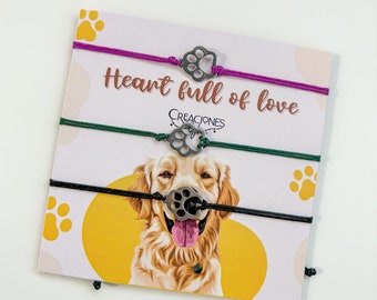 May include: Three friendship bracelets with paw print charms on a card that reads "Heart full of love". The bracelets have purple, green, and black cords. The card features a golden retriever illustration and paw prints.