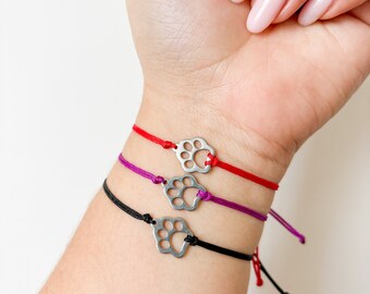 May include: Three bracelets with silver paw print charms. The bracelets are red, purple, and black.