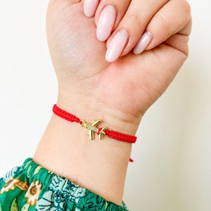 May include: Red string bracelet with a gold airplane charm. The charm has small clear rhinestones.