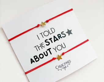 Puede incluir: Dos pulseras de cuerda roja con abalorios de estrella dorada. Las pulseras están atadas juntas y tienen el texto "I told the stars about you" impreso en una tarjeta blanca.