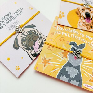 Op de afbeelding: Hondenarmbanden met gele koorden en bedels in de vorm van een pootafdruk. Elke kaart toont een illustratie van een ander hondenras, waaronder een mopshond, een golden retriever en een schnauzer. Tekst in het Spaans is zichtbaar.