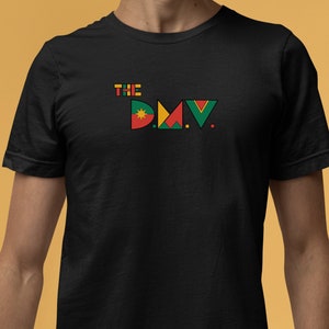 May include: Black t-shirt with a graphic design of the letters "DMV" in colorful geometric shapes and the word "THE" above it.