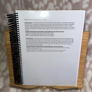 May include: A wooden desk organiser holds a spiral-bound notebook with printed text. The notebook's pages detail patient encounter summaries, including medical histories, prescriptions, and drug classes. The organiser has a natural wood finish.