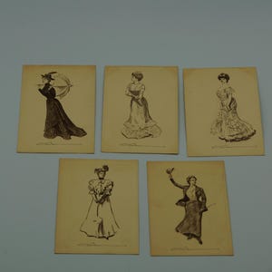 Op de afbeelding: Vijf vintage ansichtkaarten met sepia-illustraties van vrouwen in elegante kleding. Elke kaart toont een andere pose en outfit, met gedetailleerde lijntekeningen. De kaarten zijn gerangschikt op een lichtblauwe ondergrond.