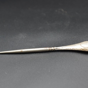 Puede incluir: Un ganchillo de plata vintage con un mango martillado y un extremo de gancho curvado. La herramienta está diseñada para trabajos de artesanía y textiles. El mango tiene una forma ovalada decorativa.