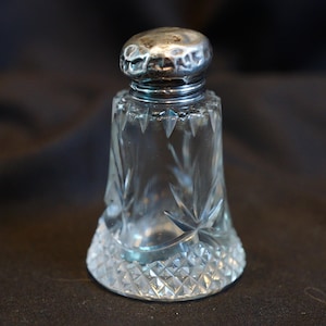 May include: A clear glass bottle with a silver top. The bottle has a diamond pattern and is empty.