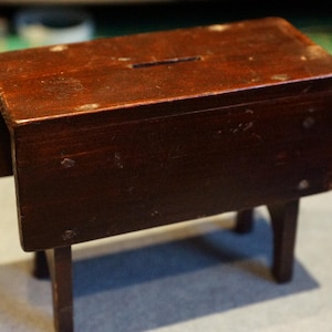 May include: A dark brown wooden folding table with a small rectangular opening in the top. The table has three legs and is made of solid wood.