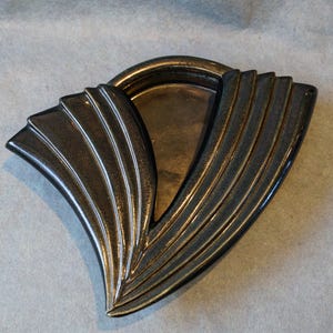 May include: A black ceramic dish with a decorative, fan-shaped design. The dish has a raised rim and a smooth, glossy finish.