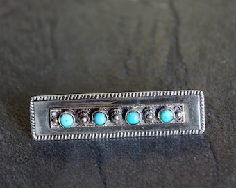 May include: A silver bar brooch with a row of turquoise stones set in a decorative border.