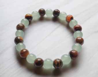 May include: A beaded bracelet featuring alternating light green and brown beads. The brown beads have a tiger-eye appearance, while the light green beads are a translucent, pale green color. The bracelet is displayed on a white surface.