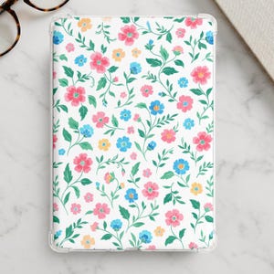 以下が含まれることがあります： 白い背景に花柄が繰り返される長方形のタブレットケース。ピンク、水色、黄色の花と緑の茎や葉が、繊細で流れるような植物の配置で描かれています。