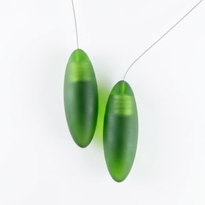 May include: Two green, oval-shaped glass beads suspended by thin, silver-colored wires. The beads have a frosted appearance and a subtle, ribbed texture near the top. The background is plain white.