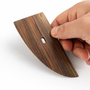 Op de afbeelding: Een donkerbruin houten polijstgereedschap met een taps toelopende, gebogen rand en een platte, brede bovenkant. Het gereedschap heeft een kleine, gecentreerde ovale uitsparing en het woord "HOHOTOOLS" verticaal in het houtnerfoppervlak gedrukt.
