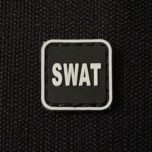 Könnte beinhalten: Ein schwarz-weißes Patch mit dem Wort "SWAT" in weißen Buchstaben auf schwarzem Hintergrund. Das Patch hat einen weißen Rand.