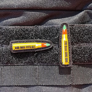 May include: Black tactical pouch with a hook and loop front panel. Two bullet-shaped patches are attached, one horizontal and one vertical, both with the text "ONE SIZE FITS ALL".