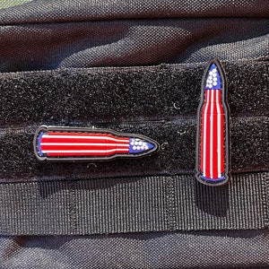 Könnte beinhalten: Eine schwarze taktische Tasche mit zwei amerikanischen Flaggen-Geschoss-Patches, die an der Vorderseite befestigt sind.