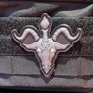 May include: A black tactical pouch with a zipper closure and a black and gray patch of a goat head with horns and a pentagram on its forehead.