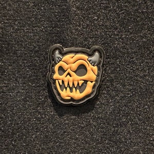 May include: A black and yellow embroidered patch featuring a cartoon devil skull design.