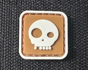 May include: A brown and white skull patch with a white outline. The patch is made of a soft, textured material and has a stitched edge.