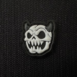 Könnte beinhalten: Ein weißer Schädel mit Hörnern und einem grimmigen Grinsen, dargestellt in einem schwarz-weißen Cartoon-Stil. Der Schädel ist schwarz umrandet und hat einen 3D-Effekt.