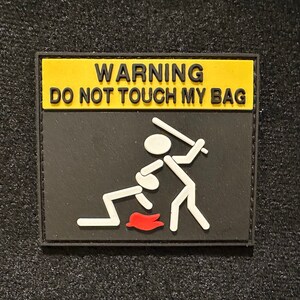Può includere: Un cartello di avvertimento nero e giallo con il testo "WARNING DO NOT TOUCH MY BAG" e un'illustrazione di un personaggio stilizzato di una persona che colpisce un'altra persona con una mazza.