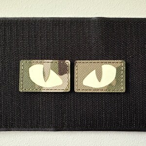 Peut inclure: Deux patchs en tissu camouflage avec des yeux blancs qui brillent dans le noir. Les patchs sont rectangulaires et ont une bordure cousue.