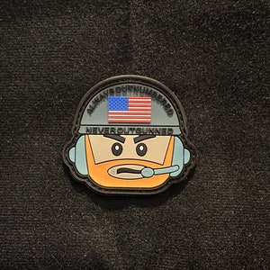 May include: A black and gray patch featuring a cartoon character wearing a helmet with the American flag. The text "ALWAYS OUTNUMBERED NEVER OUTGUNNED" is displayed around the flag and character.