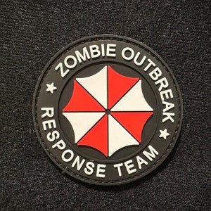 Peut inclure: Patch noir et blanc avec un motif de parapluie rouge et blanc. Le texte "Zombie Outbreak Response Team" est écrit autour du parapluie.