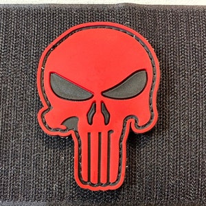Könnte beinhalten: Roter und schwarzer Totenkopf-Patch mit detailliertem Design. Der Totenkopf ist schwarz umrandet und hat eine schwarze Augenhöhle und Zähne. Der Totenkopf befindet sich auf einem schwarzen Hintergrund.