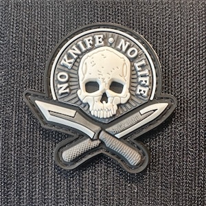 Puede incluir: Un parche bordado en blanco y negro con una calavera y huesos cruzados. El parche dice "No Knife No Life" y "Backhand".