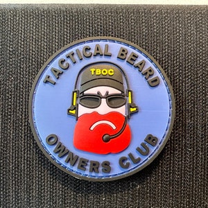 May include: A blue and black circular patch with the text "Tactical Beard Owners Club" and a cartoon image of a person with a red beard wearing a black hat and sunglasses.